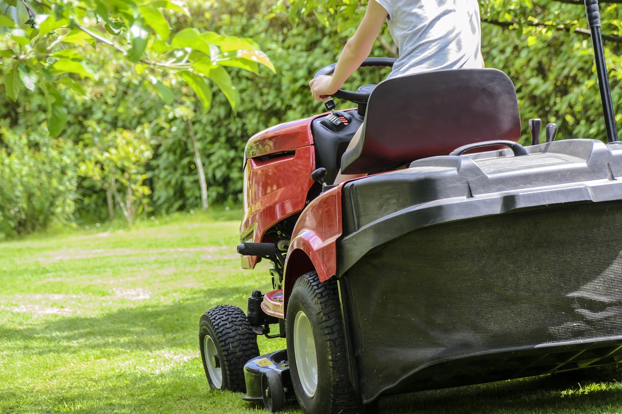 person riding a red and black lawnmower, cutting their grass